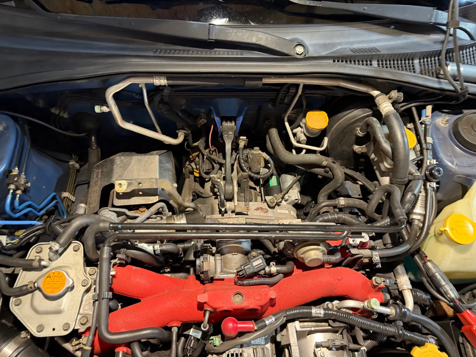 The same engine bay with the intercooler removed, exposing the throttle body, the red intake manifold, and the tangle of hoses underneath.
