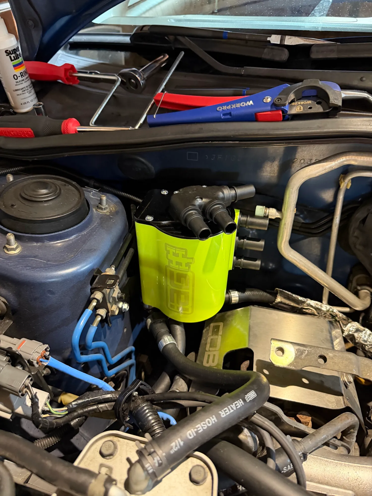 The IAG air oil separator bolted into the corner of the engine bay with hoses connected, tools resting on the strut tower above it.