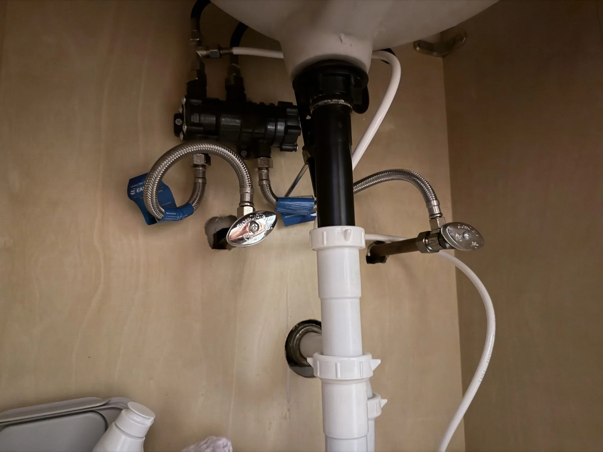 The NaviCirc valve mounted horizontally under a bathroom sink, connected by braided hoses to the hot and cold shutoff stops.