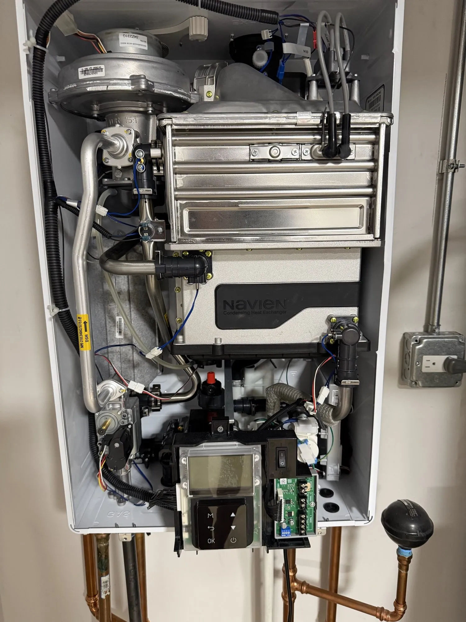 A Navien tankless water heater with its front cover removed, showing the heat exchanger, gas line, and control board.